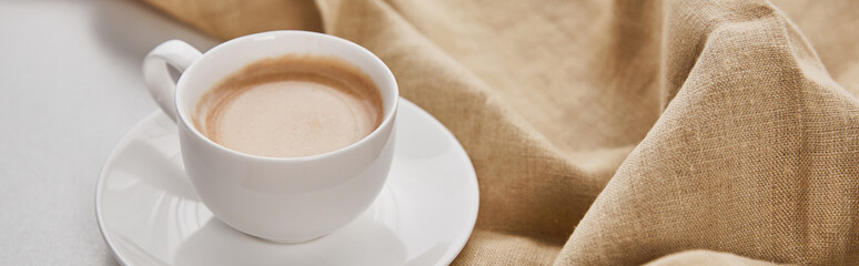 close up view of coffee in white cup on saucer near beige napkin, panoramic shot