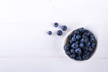 Freshly picked blueberries in bowl on white wooden background. Blueberry antioxidant. Concept for healthy eating and nutrition flat lay