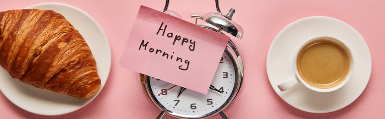 top view of alarm clock with happy morning lettering on sticky note near coffee and croissant on pink background, panoramic shot
