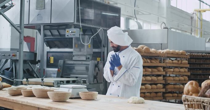 Baker with a beard dancing funny in a bakery industry kitchen while preparing the dough for baking bread, food factory