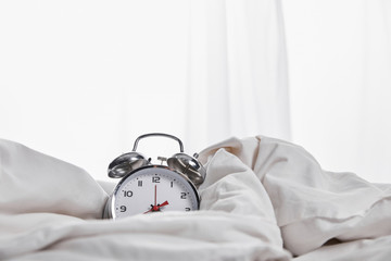 silver alarm clock covered with blanket in white bed