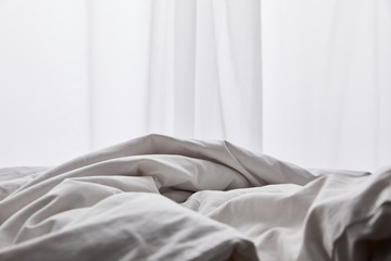 crumpled white cotton blanket in bed near curtain