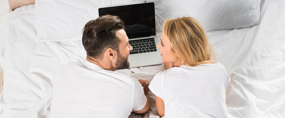 Fototapeta premium panoramic shot of couple lying in bed and using laptop at home