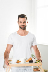 handsome man holding food tray with breakfast at home