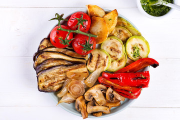 Grilled vegetables on a plate with pesto on white wooden background, flat lay