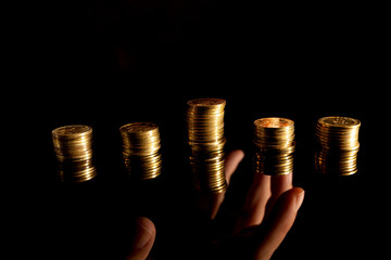 Stacks of coins on the dark background and hand reaching underneath stealing them
