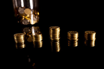Stacks of coins on the black background with jar filled with coins behind them