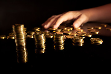 Stack of coins with pile of coins in the background and hand grabbing them