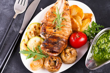 Chicken breast grill with bbq vegetables and pesto sauce in a plate on a concrete background, flat lay,