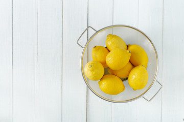 Pile of lemons in colander on a wooden table with copy space top view