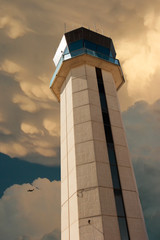 Commercial Airport Control Tower From Close Up Perspective with a strong thunderstorm overhead and commercial aircraft flying by illustrating air traffic control weather challenges.