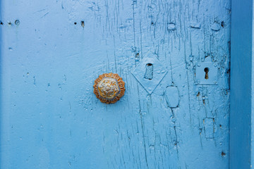 close up of an ancient metal doorknob and door lock on a weathered, shabby light blue door entrance