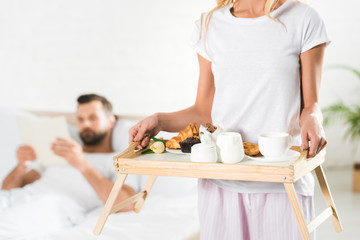 cropped view of woman holding food tray with breakfast in bedroom
