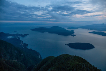 Fototapeta premium Beautiful View of Canadian Mountain Landscape covered in clouds during a vibrant summer sunset. Taken on top of St Mark's Summit, West Vancouver, British Columbia, Canada.
