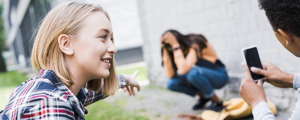 panoramic shot of african american boy and blonde teenager pointing with finger and shooting scared teenager