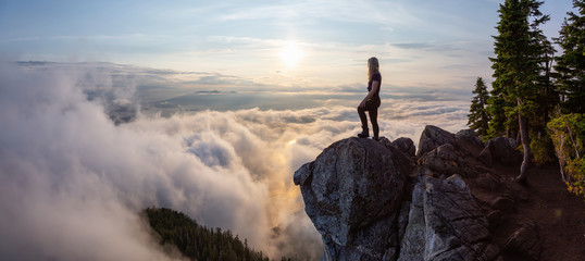 Fototapeta Adventurous Female Hiker on top of a mountain covered in clouds during a vibrant summer sunset. Taken on top of St Mark's Summit, West Vancouver, British Columbia, Canada. obraz
