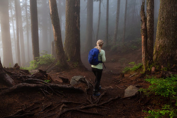 Adventurous girl hiking on a trail in the woods during a foggy and rainy day. Taken in Cypress Provincial Park, Vancouver, British Columbia, Canada.