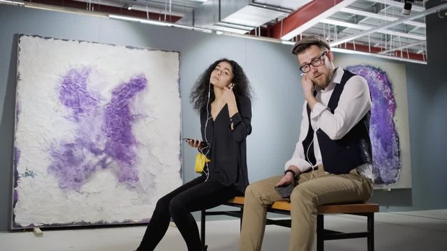 Two art lovers are enjoying modern artwork in gallery and listening audio guide