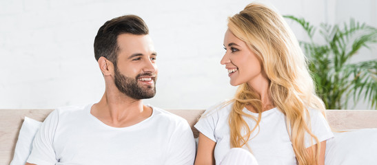 panoramic shot of beautiful couple in pajamas looking at each other on bed at home