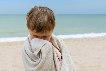 The little boy is wrapped in a towel by the sea. The concept of a child's rest on the sea.