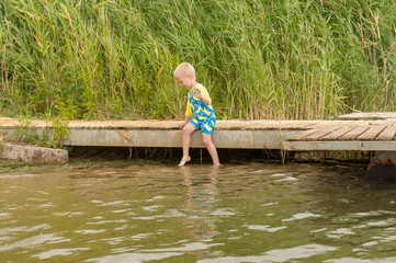 Funny children in swimsuits accelerate on wooden bridge near river and jump into water. boys are happy on holiday in village together. Summer day, river, swimming in water