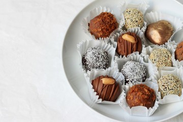Homemade chocolates in a white plate on a light background. Copy space.