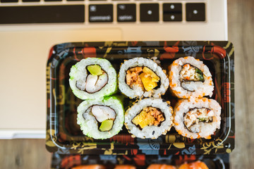 Tasty sushi rolls, shrimp and laptop at wooden table. Food delivery. Workplace at home