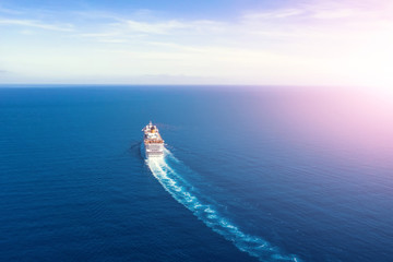 Cruise ship liner goes into horizon the blue sea leaving a plume on the surface of the water seascape during sunrise. Aerial view, concept of sea travel, cruises.