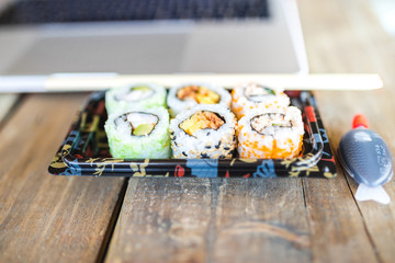 Several tasty sushi rolls and laptop at wooden table