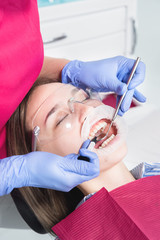 Close-up of a dentist applying polymer from a syringe to the inside of a young patient's front tooth in a dental office
