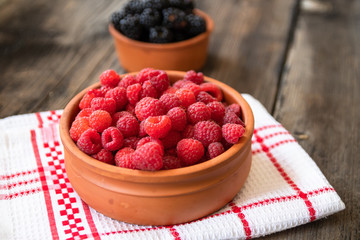 Fresh organic raspberries in a clay bowl on old wooden table