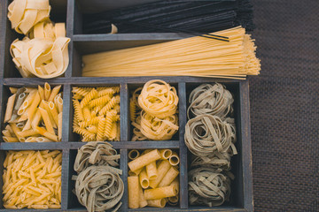 Top view Various types of Italian pasta in a wooden box with different cells.