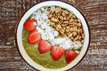 Delicious organic green smoothie bowl garnished with strawberries, sliced almonds and granola