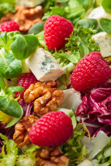 Green salad with slices of blue cheese , raspberries and nuts.