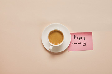 top view of coffee and sticky note with happy morning lettering on beige background
