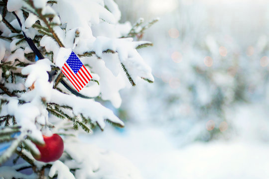 Christmas USA . Christmas tree covered with snow and a flag of United States. American flag closeup. Winter background scene outdoor. Holiday greetings card