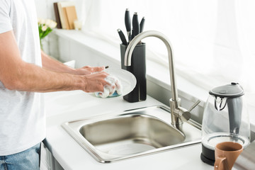 Cropped view of man washing dishes at kitchen in morning