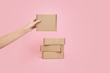 Woman's hands holding boxes stacked on pale pink background. Mock up.