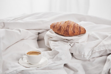 tasty croissant on plate near coffee in white cup on saucer in bed