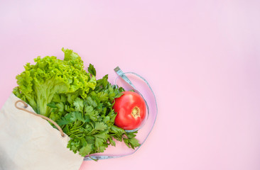 Fresh greenery and vegetables in eco bag on pink color background with copyspace. Healthy eating concept.
