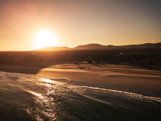 Beach and ocean during sunrise or sunset time with sun behind the mountains in background - beautiful aerial view of nature outdoors - nobody there and travel concept for wild coasts