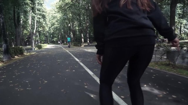 White handsom brown hair girl in tight black pants woman riding roller skates in park, during summer day