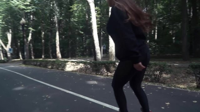 White handsom brown hair girl in tight black pants woman riding roller skates in park, during summer day