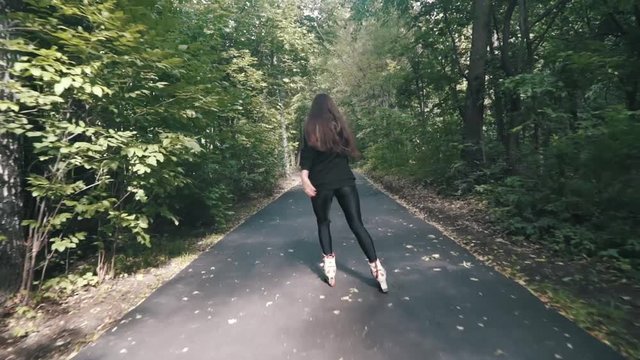 White handsom brown hair girl in tight black pants woman riding roller skates in park, during summer day