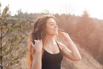 A beautiful girl in the mountains fixes her hair and enjoys the summer with her eyes closed. Sunny day