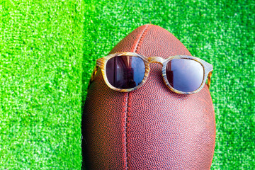 A ball for american football and summer sunglasses, funny sport concept on the green grass background