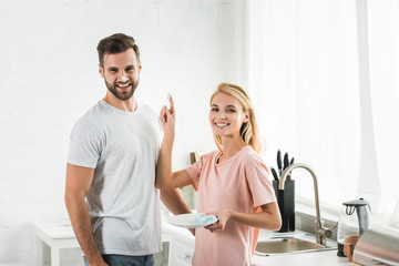 beautiful woman putting foam on smiling man at kitchen in morning