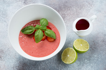 White bowl with cold strawberry cream-soup, elevated view over light-grey stone background