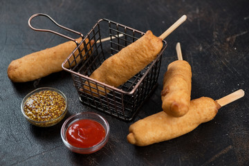 Freshly cooked deep-fried sausages with dough covering and dips over dark brown stone background