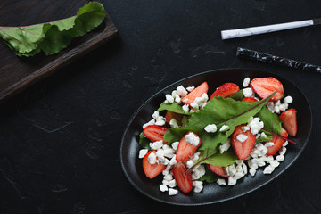 Salad with beetroot leaves, strawberries and cottage cheese. Flatlay over black stone background with copyspace